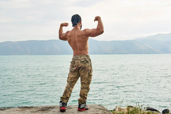 young muscular man exercising on the beach, young muscular man doing bodibuilding exercises on the beach, athletic young man posing on the beach