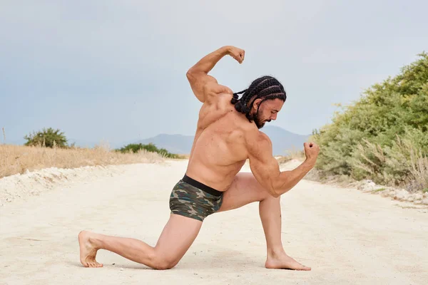 young muscular man exercising on the beach, young muscular man doing bodibuilding exercises on the beach, athletic young man posing on the beach