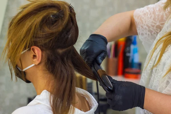 young woman with hair rollers, young woman in the hairdresser salon, the hairdresser with black protective mask decorates the client's hair