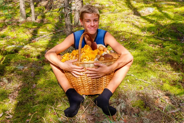 Gelukkig tiener jongen zit in de herfst bos met een grote mand van cha — Stockfoto