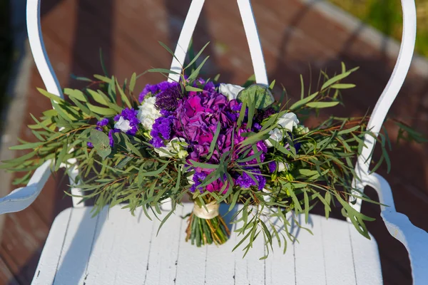 Belo buquê de casamento em uma cadeira de ferro forjado branco . — Fotografia de Stock