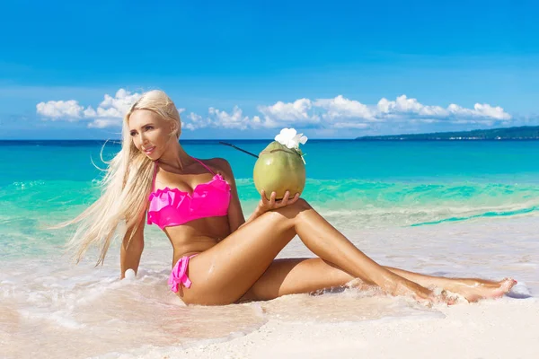 Prachtige blondine met lang haar in bikini met kokosnoot op een trop — Stockfoto