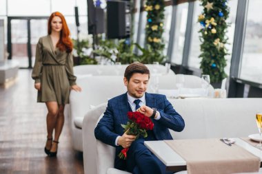 Genç beyaz adam restoranda kız arkadaşını bekliyor.