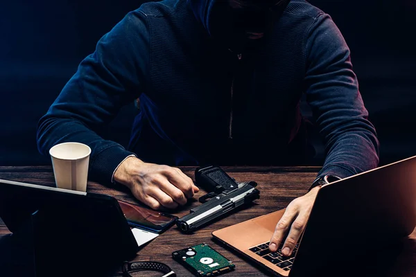 Обрезанный человек с пистолетом и ноутбуком — стоковое фото