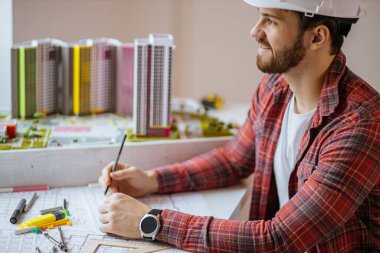 Genç inşaatçı ofiste proje üzerinde çalışıyor.