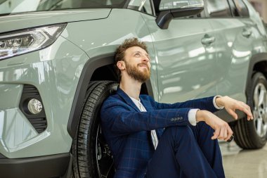 smiling guy sitting on the floor next to automobile