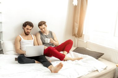Kafkasyalı eşcinseller dizüstü bilgisayar kullanarak yatakta otururlar.