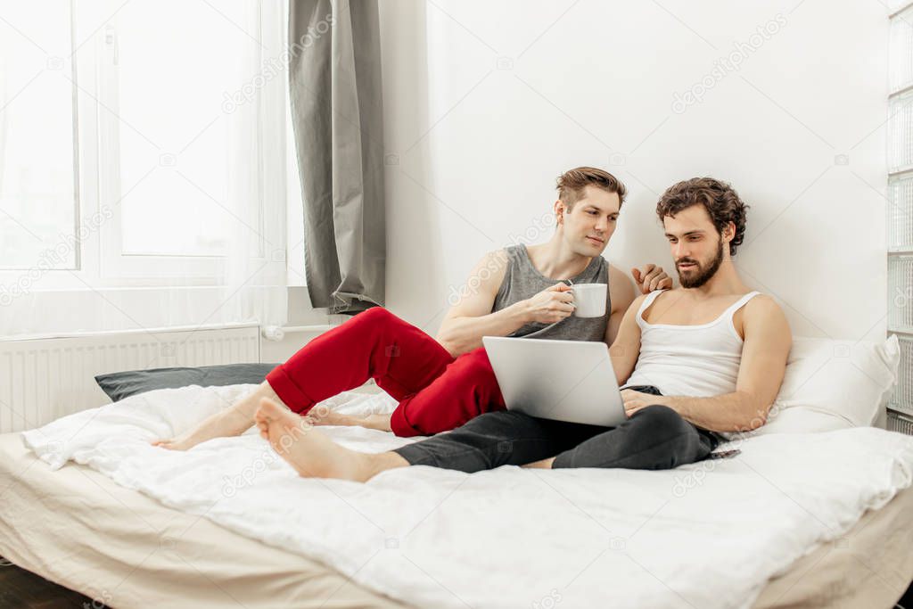 caucasian gays sit on bed using laptop