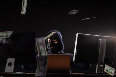 Maskeli genç hacker para dolu uzayda oturuyor.