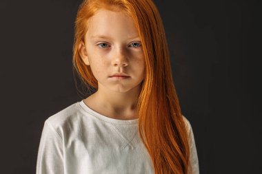 portrait of serious redhaired girl isolated over black background