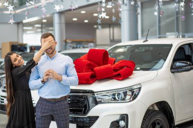 beautiful woman closed husbands eyes, going to make surprise in dealership