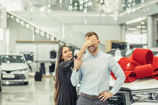 Beautiful woman closed husbands eyes, going to make surprise in dealership — Stockfoto