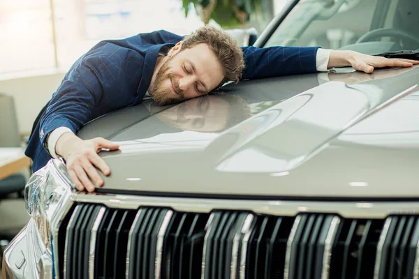 Positivo jovem cara abraçando carro na concessionária — Fotografia de Stock