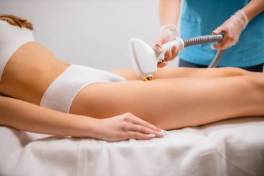 slender female lie on bed while getting laser epilation on hips