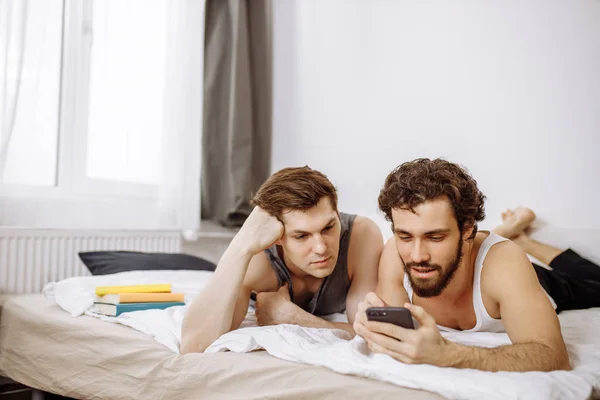 Lovely caucasian gays on bed, use mobile phone — Zdjęcie stockowe