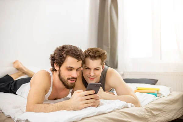 Gays acostados en la cama con smartphone — Foto de Stock