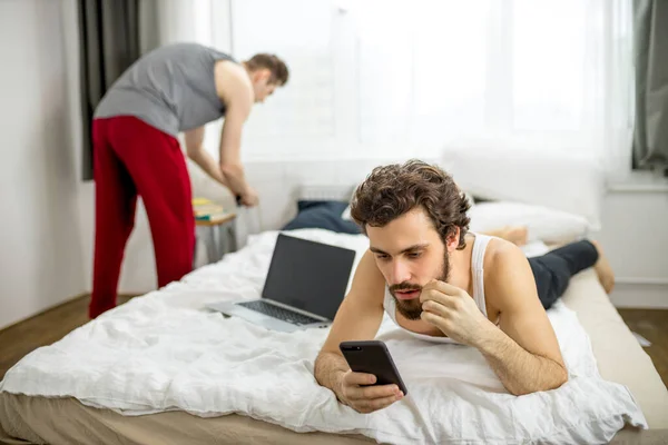 Caucasian gays lying on bed using laptop and smartphone — Zdjęcie stockowe