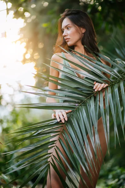 Slender young lady covering body with green plant — Stok fotoğraf