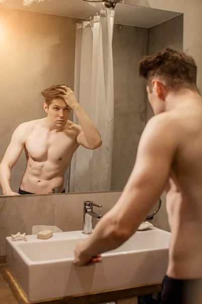 Muscular handsome guy looking at his reflection on mirror — Stockfoto