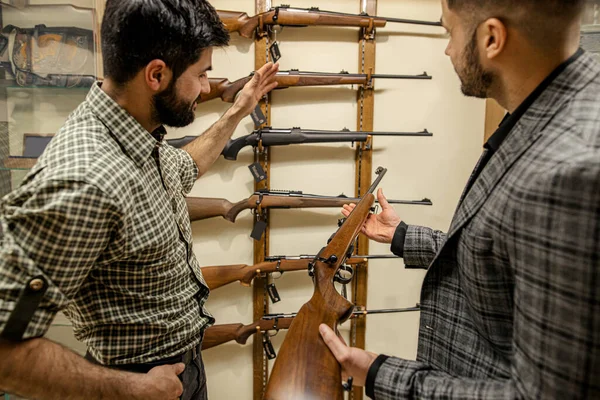 Jovem vendedor ajudando cliente a escolher arma na loja de armas — Fotografia de Stock