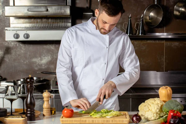 Joven cocinero profesional cortar verduras frescas en la cocina — Foto de Stock