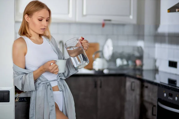 Jeune femme verser de l'eau dans la cuisine — Photo