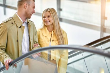 Genç çift alışveriş merkezinde yürüyen merdivene tırmanıyor.