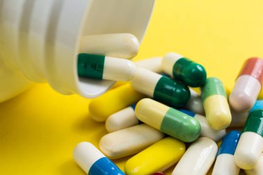 Sarı masadaki kapsül yığını. Şişeler tabletlerden dökülüyor.. 