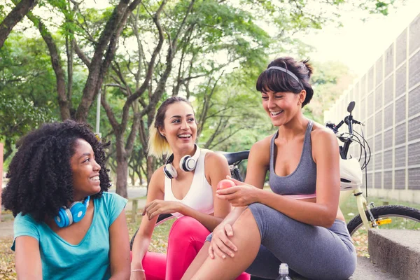 Group of sporty female friends bonding and laughing. Women hanging out and having fun while relaxing, resting after training. Trees in background.