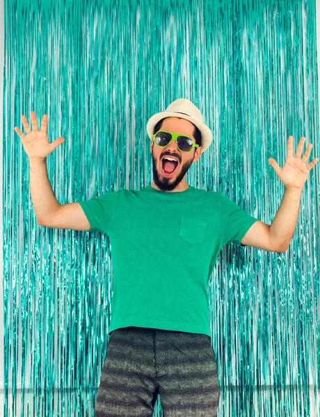 Man screaming and celebrating. Carnival in Brazil, birthday party, eve of the end of the year. Green clothes, sunglasses, white panama hat. Colored background.