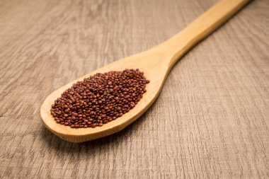 Chenopodium kinoa, Kırmızı kinoa tohumunun bilimsel adıdır. Tahta masanın üzerinde kaşık ve tahıllar.