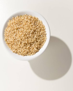 Oryza sativa, tüm Short Grain Rice Seed 'in bilimsel adıdır. Sushi Rice ve Arroz Cateto Integral (Portekizce) olarak da bilinir. Kasedeki tahıllar. Beyaz masanın üzerindeki gölge.