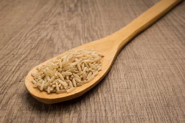 全麦稻种的学名是全麦稻种 也被称为长谷米和Arroz Agulha Integral 葡萄牙语 木桌上的勺子和谷粒 — 图库照片