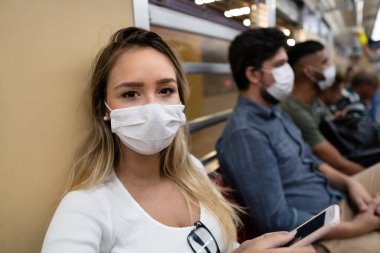 Genç kadın vagonun içinde cep telefonu kullanıyor. Gezgin CoroVirüs bulaşmasını önlemek için maske takıyor, Covid-19.