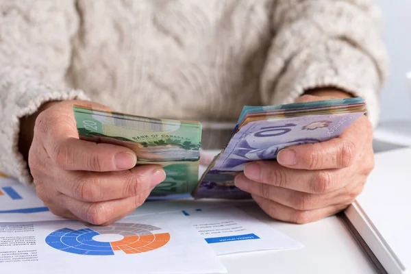 Money from Canada. Dollars. Canadian currency. Retired woman holding bill on desk office.