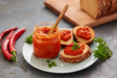 Ajvar (biber köpük) bir kavanoz ve bir dilim ekmek. Ajvar - kırmızı biber, soğan ve sarımsak lezzetli yemek.