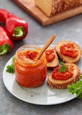 Ajvar (biber köpük) bir kavanoz ve bir dilim ekmek. Ajvar - kırmızı biber, soğan ve sarımsak lezzetli yemek.