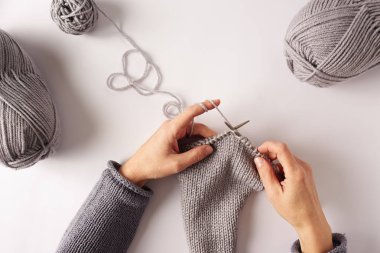 Top view of female hands knitting with grey wool on white background clipart