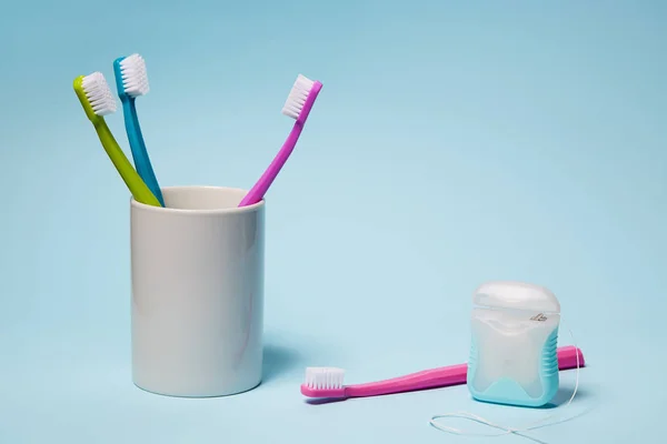 Bunte Zahnbürsten Becher Und Zahnseide Auf Hellblauem Hintergrund — Stockfoto