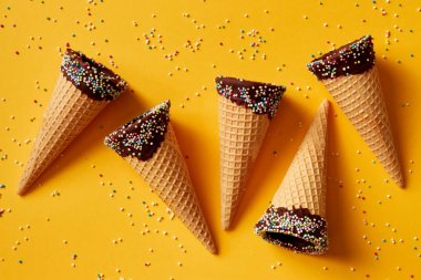 Sarı arka plan üzerinde renkli sprinkles ile dondurma koniler. 
