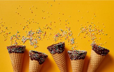 Sarı arka plan üzerinde renkli sprinkles ile dondurma koniler. 