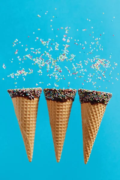 Ice cream cones with colorful sprinkles on blue background.