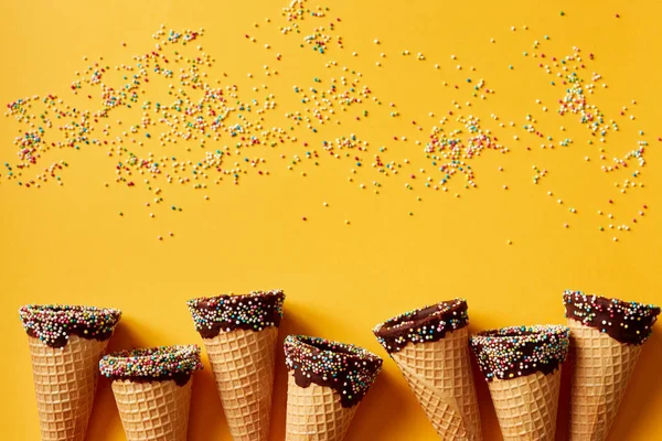 Ice cream cones with colorful sprinkles on yellow background.