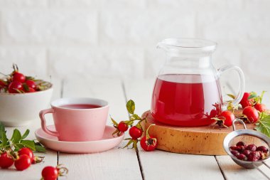 Bir fincan gül kalçası çayı ve yanında taze gül kalçası.