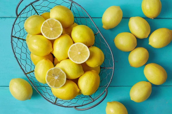 蓝色桌子上的铁丝篮里有新鲜的柠檬 — 图库照片