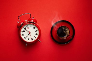 Kırmızı arka planda retro alarm saati olan bir fincan sıcak kahve.. 