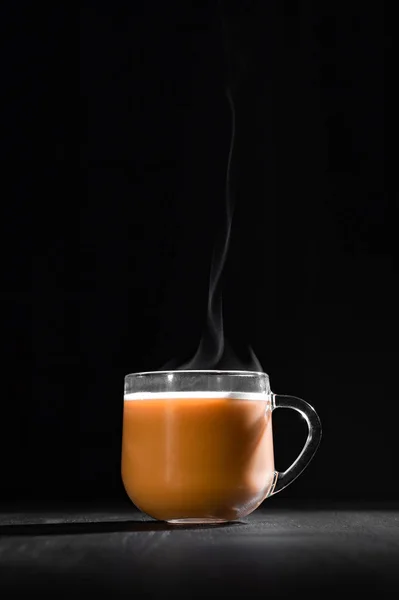 Hot cocoa with milk in a transparent mug with steam on a black background with a place for inscription — Stock Photo, Image
