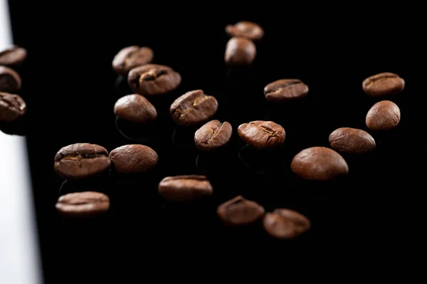 Grains de café torréfiés reposent sur verre noir gros plan. contexte — Photo