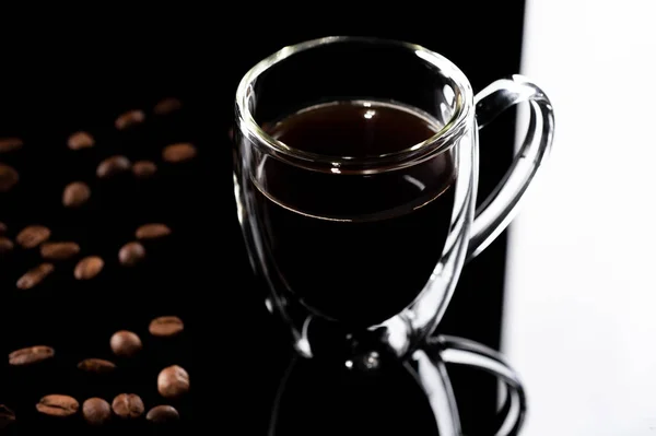 Verificador de vidro com café preto em um fundo de vidro preto. grão de café ao lado do copo — Fotografia de Stock