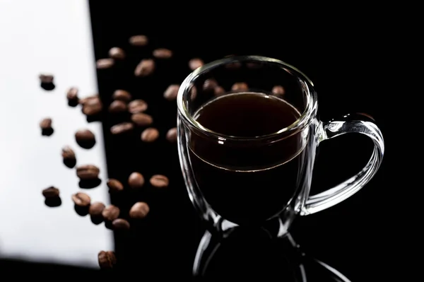 Verificador transparente com café em um fundo de vidro preto. grão de café é espalhado ao lado da xícara — Fotografia de Stock